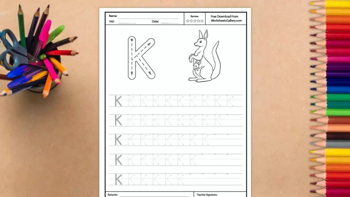 A black and white educational worksheet for tracing the uppercase letter K, featuring an illustration of a mother kangaroo with a joey in her pouch, surrounded by a desk setup with colorful
