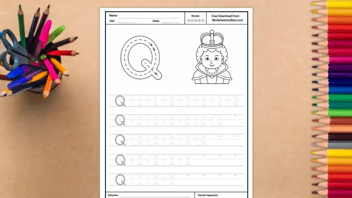A full view of an educational worksheet for the letter Q, placed on a light wooden background between a jar of pens and a row of colored pencils. The page features a large Q with directional