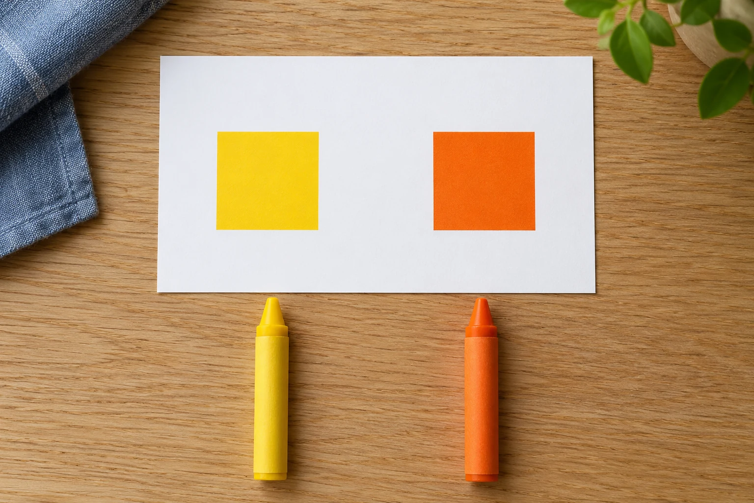 Check whether the reference colours remain distinct Yellow and orange square swatches sit on a white card above matching yellow and orange crayons on an oak table.
